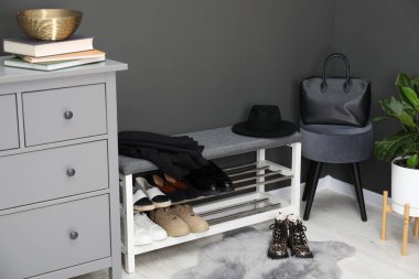 Ayakkabı bankı, farklı ayakkabılar, aksesuarlar ve kapalı alandaki gri duvarın yanındaki bitki örtüsü.