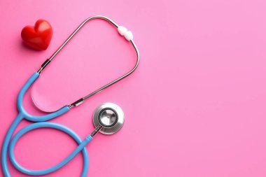 Pembe arka planda steteskop ve kırmızı kalp. Metin için boşluk