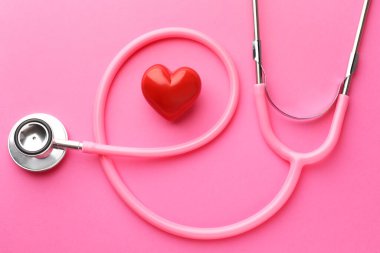 Pembe arka planda steteskop ve kırmızı kalp, düz yatıyordu.