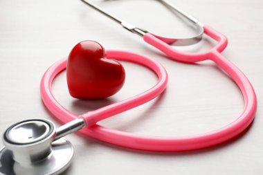 Pembe steteskop ve kalp modeli açık ahşap masada, yakın plan.