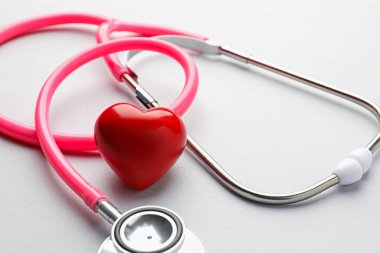 Açık gri arka planda pembe steteskop ve kalp modeli, yakın plan.