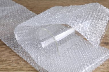 Baloncuk ambalajı ve cam deney şişesi ahşap masada, yakın plan.