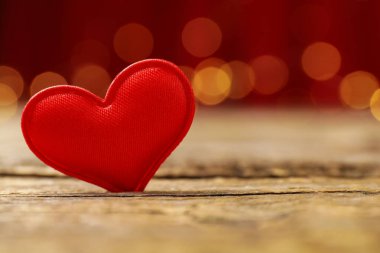 Sevgi. Ahşap masada kırmızı dekoratif kalp bulanık ışıklara karşı, yakın plan. Metin için boşluk