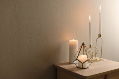 Bej duvarın yanındaki ahşap masada şamdanların içinde yanan mumlar. Metin için boşluk