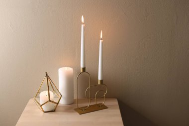 Bej duvarın yanındaki ahşap masada şamdanların içinde yanan güzel mumlar.
