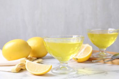 Tatlı kaselerinde leziz sarı jöle ve beyaz mermer masada taze limonlar, yakın plan.