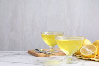 Tatlı kaselerinde leziz sarı jöle ve beyaz mermer masada taze limonlar, yakın plan. Metin için boşluk