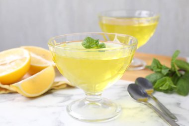 Tatlı kaselerinde leziz sarı jöle, beyaz mermer masada taze limon, yakın plan.