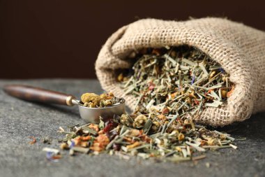 Torbada kurutulmuş bitki çayı ve gri masada ölçü kaşığı, yakın plan.