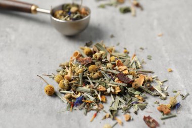 Açık gri masada kurutulmuş bitki çayı ve ölçü kaşığı, yakın plan.