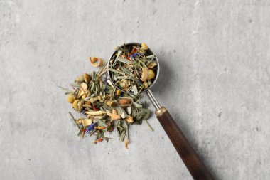 Açık gri masada kurutulmuş bitki çayı ve ölçü kaşığı.