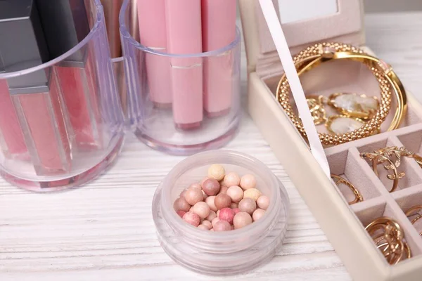Makyaj ürünleri tutacaklarda ve farklı altın mücevher kutularında açık ahşap masada, yakın plan.