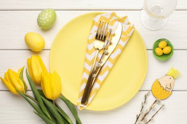 Paskalya kutlaması. Çatal bıçak takımları, söğüt dalları, çiçekler ve beyaz ahşap masaya boyanmış yumurtalar.