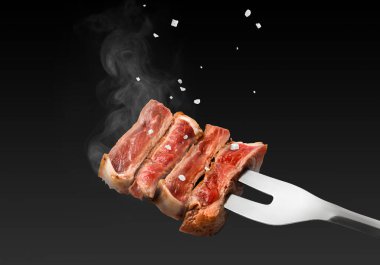 Et çatalı üzerine sığır eti parçaları ve siyah arkaplan üzerine düşen tuz