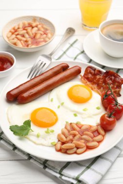 Geleneksel İngiliz kahvaltısı. Lezzetli, güneşli, pastırmalı yumurta ve sosisler beyaz ahşap masada servis ediliyor, yakın plan.
