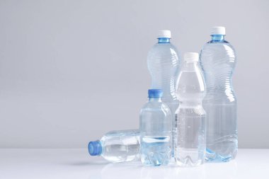 Beyaz masada gri arkaplan ile farklı boyutlarda su şişeleri, metin için boşluk