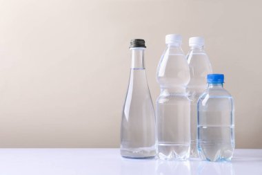 Beyaz masada bej arka planda farklı boyutlarda su şişeleri var. Metin için boşluk