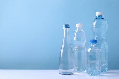 Beyaz masada açık mavi arka planda farklı boyutlarda su şişeleri var. Metin için boşluk