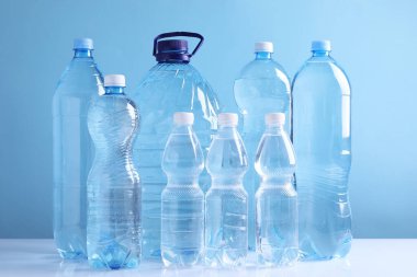 Açık mavi arka planda beyaz masada farklı boyutlarda su şişeleri