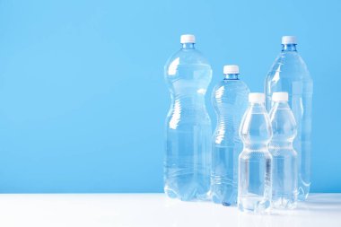 Beyaz masada farklı boyutlarda su şişeleri açık mavi arkaplan, metin için boşluk