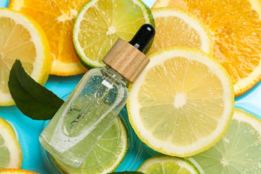 Bir şişe cilt bakımı ürünü, narenciye dilimleri ve açık mavi arkaplanda yeşil yaprak, düz bir zemin.