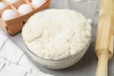 Taze hamur mayası kasede, yumurtalarda, bir bardak suda ve gri masada merdane, yakın plan.