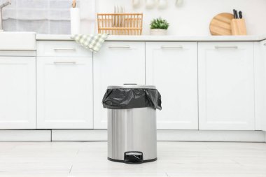 Mutfakta yerde plastik torba olan metal çöp kutusu.