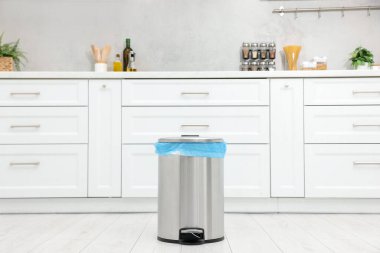 Mutfakta yerde plastik torba olan metal çöp kutusu.