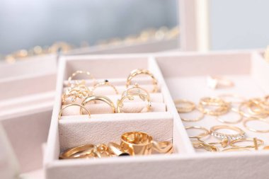 Bulanık gri arkaplan ve seçici odaklanma karşısında farklı altın mücevherlere sahip bej tepsi