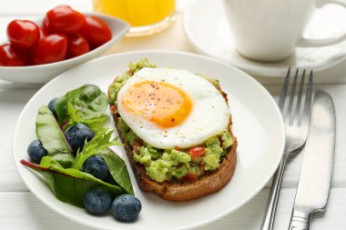Beyaz ahşap masada servis edilen avokado tostlu sağlıklı bir kahvaltı.