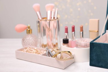 Makyaj ürünleri tutacaklarda ve mücevher kutusu açık ahşap masada gri arka planda, yakın plan. Bokeh etkisi