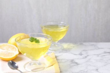 Tatlı kaselerinde lezzetli sarı jöle, nane ve taze limonlar beyaz mermer masada, yakın plan. Metin için boşluk