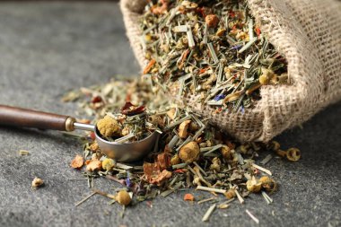 Torbada kurutulmuş bitki çayı ve gri masada ölçü kaşığı, yakın plan.