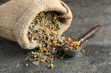 Torbada kurutulmuş bitki çayı ve gri masada ölçü kaşığı, yakın plan.