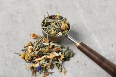 Açık gri masada kurutulmuş bitki çayı ve ölçü kaşığı, yakın plan.