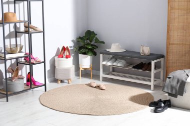 Ayakkabı bankı, farklı ayakkabılar, raf ünitesi, aksesuarlar ve açık gri duvarın yanındaki ev bitkisi.