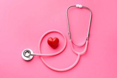Pembe arka planda steteskop ve kırmızı kalp, düz yatıyordu.