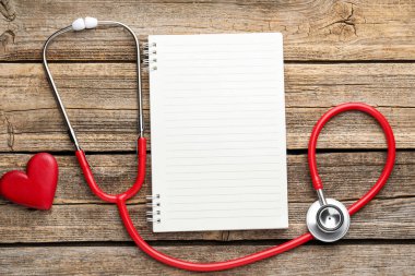 Kırmızı steteskop, not defteri ve kalp modeli tahta masada, düz yerde. Metin için boşluk