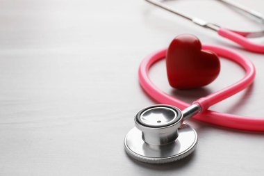 Pembe steteskop ve kalp modeli açık tahta masada, yakın plan. Metin için boşluk