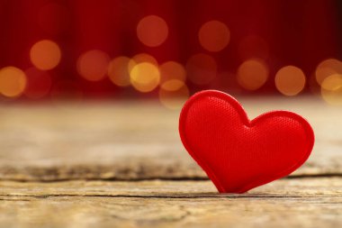 Sevgi. Ahşap masada kırmızı dekoratif kalp bulanık ışıklara karşı, yakın plan. Metin için boşluk
