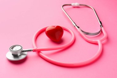 Pembe arka planda steteskop ve kırmızı kalp, yakın plan.