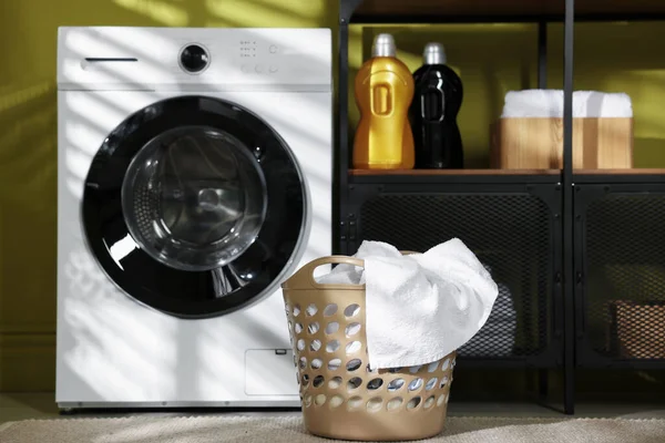 Çamaşır sepetinin içinde çamaşır makinesi ve deterjan var.