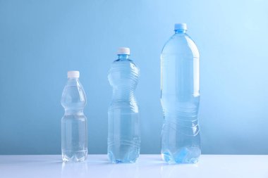 Açık mavi arka planda beyaz masada farklı boyutlarda su şişeleri