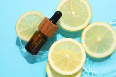 Bir şişe kozmetik ürünü ve limon dilimleri açık mavi arka planda, düz yerde.