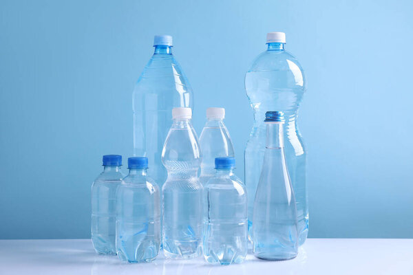 Water bottles of different sizes on white table against light blue background