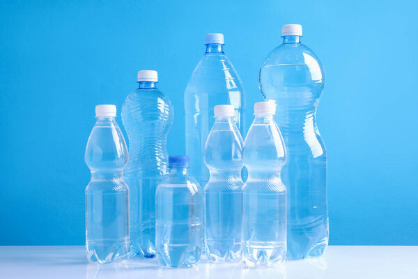 Water bottles of different sizes on white table against light blue background