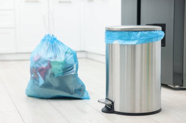 Mutfakta yerde çöp olan metal çöp kutusu ve plastik torba.