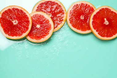 Turkuaz arka planda greyfurt dilimleri, düzlük. Metin için boşluk