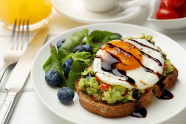Beyaz ahşap masada servis edilen avokado tostlu sağlıklı bir kahvaltı.
