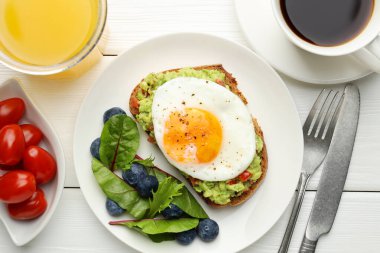 Beyaz ahşap masada servis edilen avokado tostlu sağlıklı bir kahvaltı.